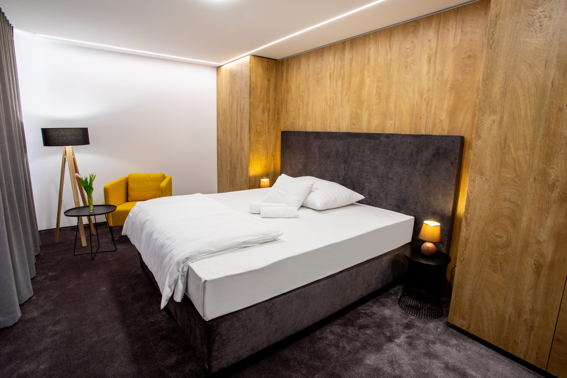 Nowoczesny pokój hotelowy z łóżkiem kontynentalnym, tapicerowanym wezgłowiem i drewnianą ścianą