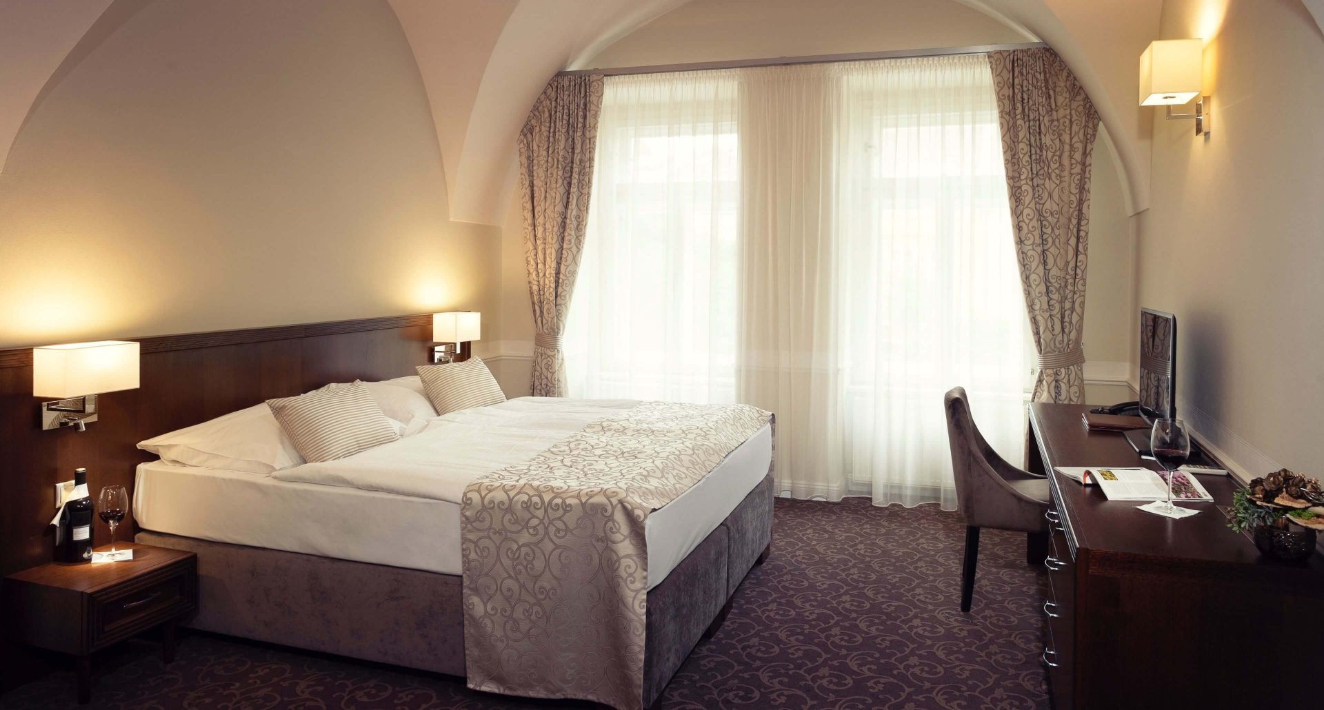 Elegancki pokój hotelowy z dużym łóżkiem, klasycznym wezgłowiem, zasłonami i biurkiem