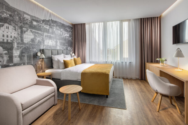 Nowoczesny pokój hotelowy z łóżkiem tapicerowanym, sofą, biurkiem i żółtymi dodatkami