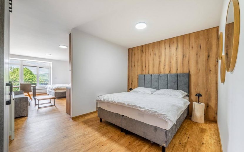 Moderní hotelový pokoj s manželskou postelí, dřevěným obkladem a výhledem